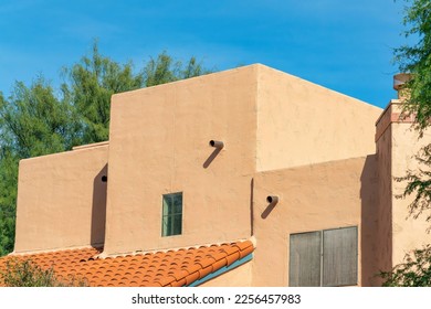 Block style building with adobe design or architecture with flat roof and red tiles and back or front yard trees in sun. Late afternoon with neighborhood in desert with mexican design on structure.