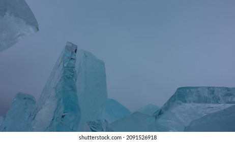 A block of turquoise hummocks on the background of a cloudy sky. Thick shiny ice floes stand upright, in disarray. Close-up. Full screen. Copy space.Baikal