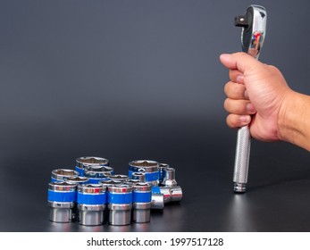 block wrench set and the hand of a man holding a ratchet wrench on a black background.