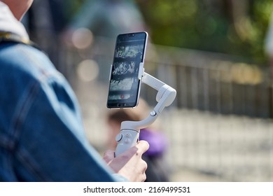 Blogger filming outdoor event on smartphone with gimbal stabilizer, video blogging for new followers. Video shooting content for social media networks, vlog video making