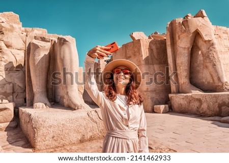 A blogger girl takes a selfie against the ruins of the grandiose Karnak temple in the ancient city of Luxor in Egypt