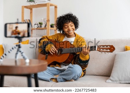 Blogger guitarist. Happy african american girl blogger playing guitar singing song recording vlog. Social media influencer woman streaming recording at home studio. Music content creator broadcast