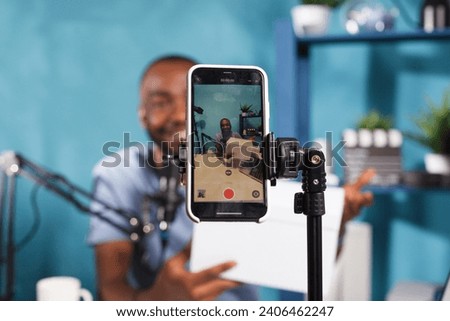 Blogger making giveaway while live streaming on smartphone screen closeup. Web content creator announcing contest and showing prize gift using mobile phone on tripod for video recording