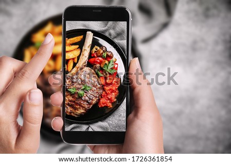 Blogger taking picture of delicious grilled ribeye at table, closeup. Food photography