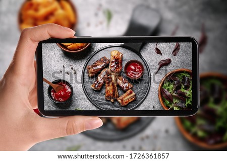 Blogger taking picture of delicious grilled ribs at table, closeup. Food photography