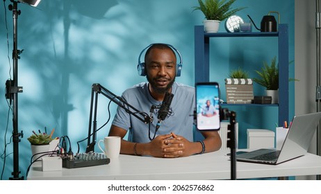Blogger waving at smartphone camera for social media vlog. Influencer using mobile phone to record podcast for channel and subscribers. Vlogger filming video with modern equipment - Shutterstock ID 2062576862