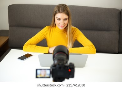 Blogger woman talking on video camera. Beautiful young blonde female filming video blog footage at home during lockdown. Entrepreneur person doing distant work online