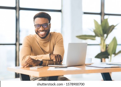 Blogger At Work. Smiling black man looking at camera, sitting at desk with laptop. Selective focus