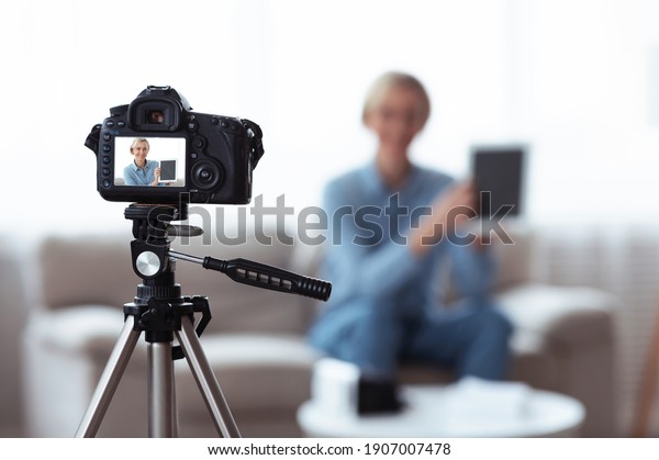 Blogging
and social media marketing concept. Millennial female influencer
recording video content for her blog, advertising new touch pad.
Focus on camera with preview screen, copy
space