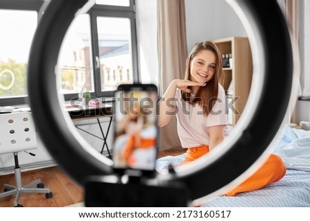 blogging, technology and people concept - happy smiling girl blogger with ring light and smartphone streaming at home
