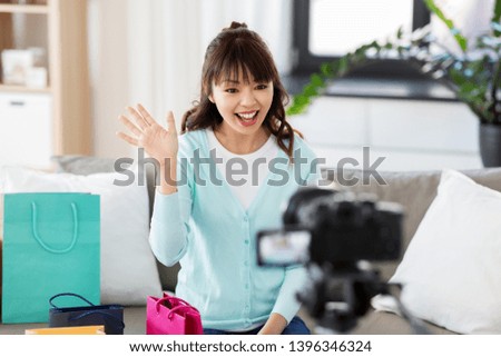blogging, technology, videoblog and people concept - happy smiling asian woman or blogger with shopping bags recording video blog by camera and waving hand at home
