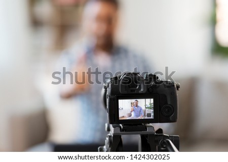 blogging, videoblog and people concept - camera recording video blog of indian male blogger showing thumbs up at home