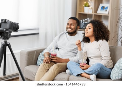 blogging, videoblog and people concept - happy african american couple of video bloggers with camera and smoothie drinks videoblogging at home - Shutterstock ID 1541446733