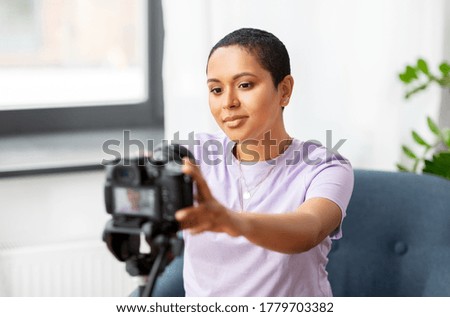 blogging, videoblog and people concept - happy african american female video blogger adjusting camera on tripod at home