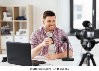 blogging, videoblog and people concept - male blogger with camera recording video review of wireless microphone at home office