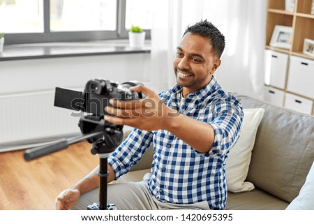 blogging, videoblog and people concept - smiling indian male video blogger adjusting camera at home