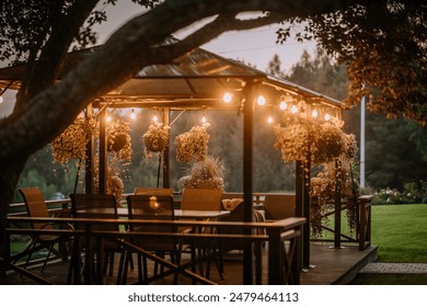 Blome, Latvia - September 11, 2023 - A cozy outdoor gazebo with hanging plants and string lights at dusk, surrounded by greenery, creating a warm and inviting atmosphere