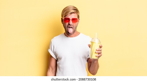 Blond Adult Man With Cheerful And Rebellious Attitude, Joking And Sticking Tongue Out With A Milkshake