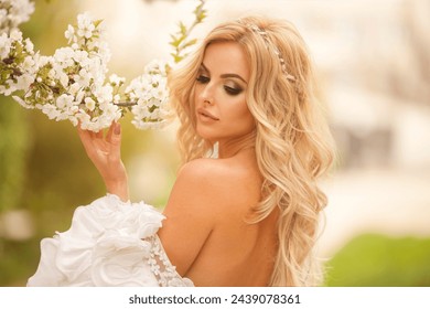 Blond blooming garden. A woman in a white dress walks through a blossoming cherry orchard. spring photo - Powered by Shutterstock