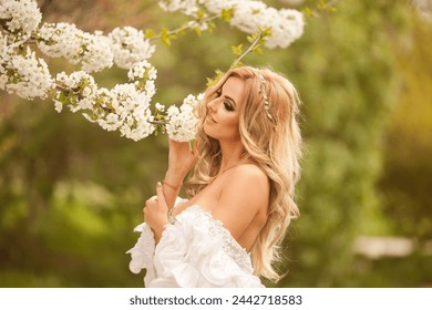 Blond blooming garden. A woman in a white dress walks through a blossoming cherry orchard. spring photo - Powered by Shutterstock