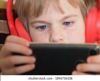 Blond Boy 6 Years Old In Red Headphones Plays A Smartphone