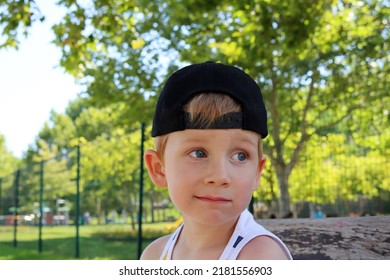 A Blond Boy With A Black Cap And A Smirk On His Face. A Thoughtful Five-year-old Boy. 