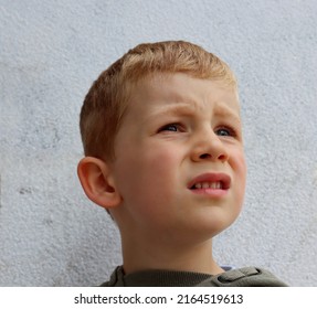 A blond boy frowns and looks off into the distance . The five-year-old boy frowned his eyebrows and squinted his eyes.  - Shutterstock ID 2164519613