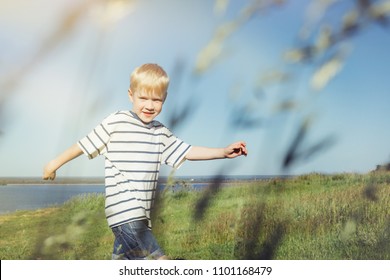 Blond Boy Joyful And Running On Nature. Field With High Grass. Conceptual Realism.