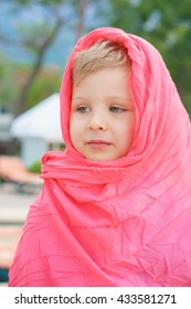 Blond boy looking to the side, wrapped in red pareo for protection from the sun. Close up. Resort on the blurry background.