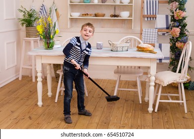 Blond Boy Sweeping The Floor In The Kitchen. Pretty Boy Helps Parents With Housework. Child Cleaning Room With Broom. Child Cleaning Kitchen. Housekeeping Concept.