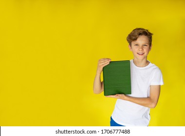 Blond Boy In White T-shirt Holding A Green Book On The Yellow Background