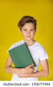 Blond Boy In White T-shirt Holding A Green Book On The Yellow Background