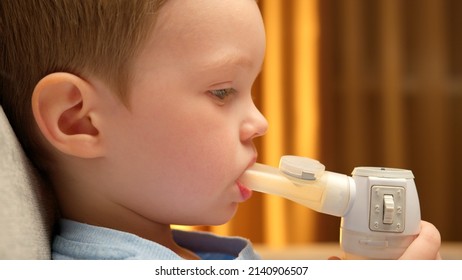 Blond Caucasian Child With Asthma Problems Inhales With Tube In His Mouth. Child Has Respiratory Infection Or Bronchitis, And He Is Breathing Heavily. Treatment Of Pneumonia With Nebulizer At Home.