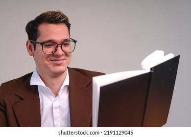 A Blond, Caucasian Man Reading A Book With A Happy Face. Man Enjoying While He Reads A Book. Man In A Suit Reading A Black Book. Happy Businessman