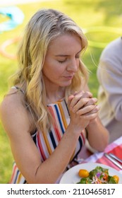 Blond caucasian woman with hands clasped and eyes closed praying at table. people and spirituality concept, unaltered.