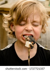 Blond Child Eating Burnt Toasted Marshmellow Off A Stick