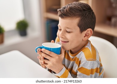 Blond Child Smelling Milk Sitting On Table At Home