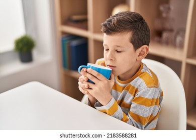 Blond Child Smelling Milk Sitting On Table At Home