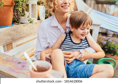 Blond curly woman hugging, caressing and playing with her child outdoor at open air terrace or backyard. Relations, happiness moments, emotion, love, education concept.