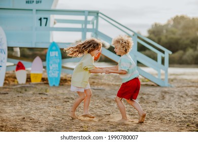 Blond schwach junge Junge und Mädchen in Sommerkleidung spielen am Sandstrand gegen blauen Rettungsturm mit Surfbrettern. Sommerzeit.