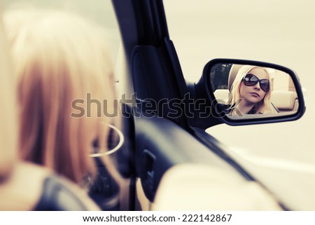 Blond fashion woman in sunglasses looking in the car mirror 