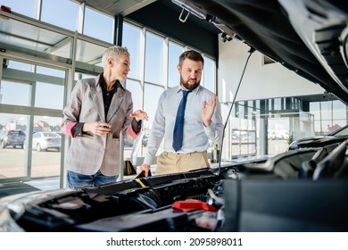 Blond female driver being concentrated while looking at the engine in dealership and open the hood of a car in showroom vehicle salon store motor showroom..