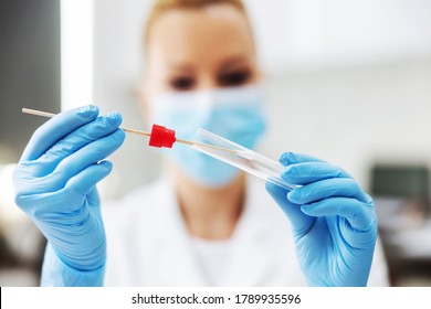 Blond female lab assistant in sterile uniform with rubber gloves and surgical mask on holding cotton swab. Laboratory interior. - Shutterstock ID 1789935596