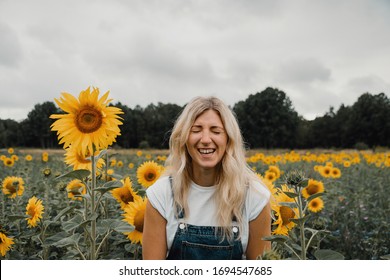 A blond girl on a sunflower field with a denim overall laughing