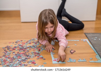 Blond girl in a pink sweater playing with a jigsaw on the floor by the confinement of coronavirus covid-19
