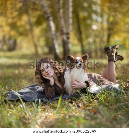 Blond girl with a small dog on a meadow in the autumn forest