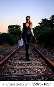 Blond Girl With Suitcase Walking On The Abandoned Railway. Sexy Woman In Black Leather Clothes With Gun At Night. Criminal Gangsta Woman Escape From Mafia. Secret Agent With Weapon.