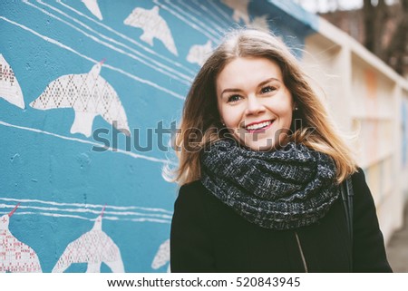 A blond girl with a warm scarf and bright lipstick on walking at city streets and laughing