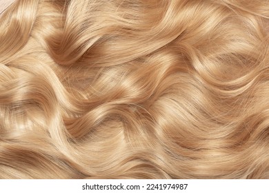 Blond hair close-up as a background. Women's long blonde hair. Beautifully styled wavy shiny curls. Hair coloring. Hairdressing procedures, extension. - Shutterstock ID 2241974987