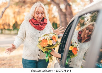 Blond hair excited middle-aged lady looking surprised at the flower bouquet given by her man who sits in a car - spring, date and women’s day celebration concept - Powered by Shutterstock